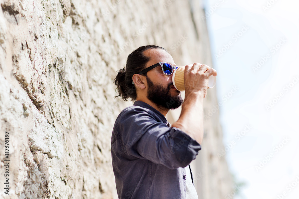man drinking coffee from paper cup on street