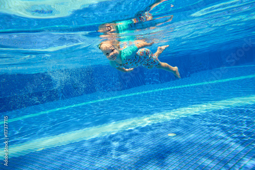 Little girl swimming underwater in the pool and smiling