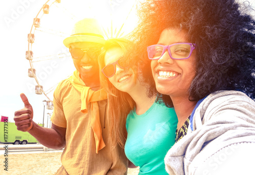 Afro hair girl taking selfie with best friends at ferris wheel at sunset - Happy multiracial group of students having fun with smartphone photo camera outside- Warm sun halo filter with vintage tones