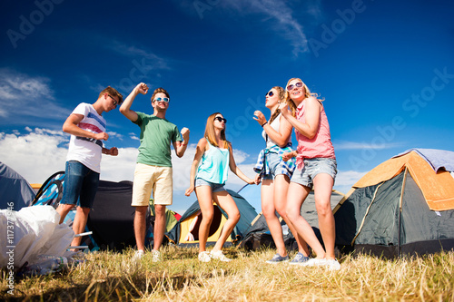 Group of teenagers at summer music festival dancing, tents