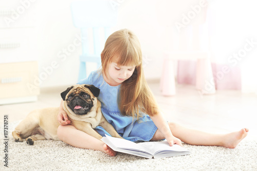 Cute girl reading book with dog on carpet