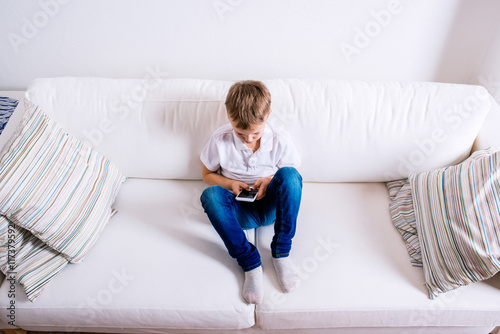 Little boy sitting on sofa, playing with smartphone