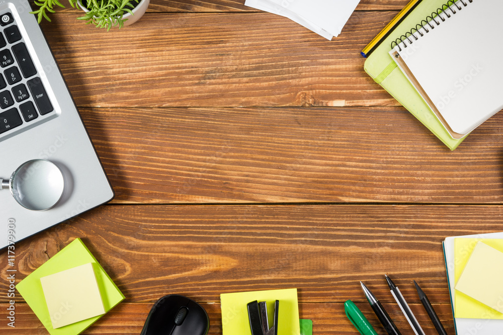 Office table desk with set of colorful supplies, white blank note pad, cup, pen, pc, crumpled paper, flower on wooden background. Top view and copy space for ad text Office table desk with set of colorful supplies, white blank note pad, cup, pen, pc, crumpled paper, flower on wooden background. Top view and copy space for ad text