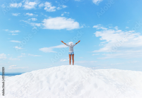 Young woman standing on white beach with her arms outstretched. She is looking towards the horizon.