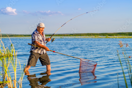 a fisherman with a fishing rod and a net is catching something in the river on a nice sunny day