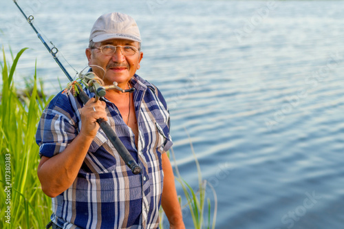 a smiling fisherman with a fishing rod is standing by the river on a nice sunny day