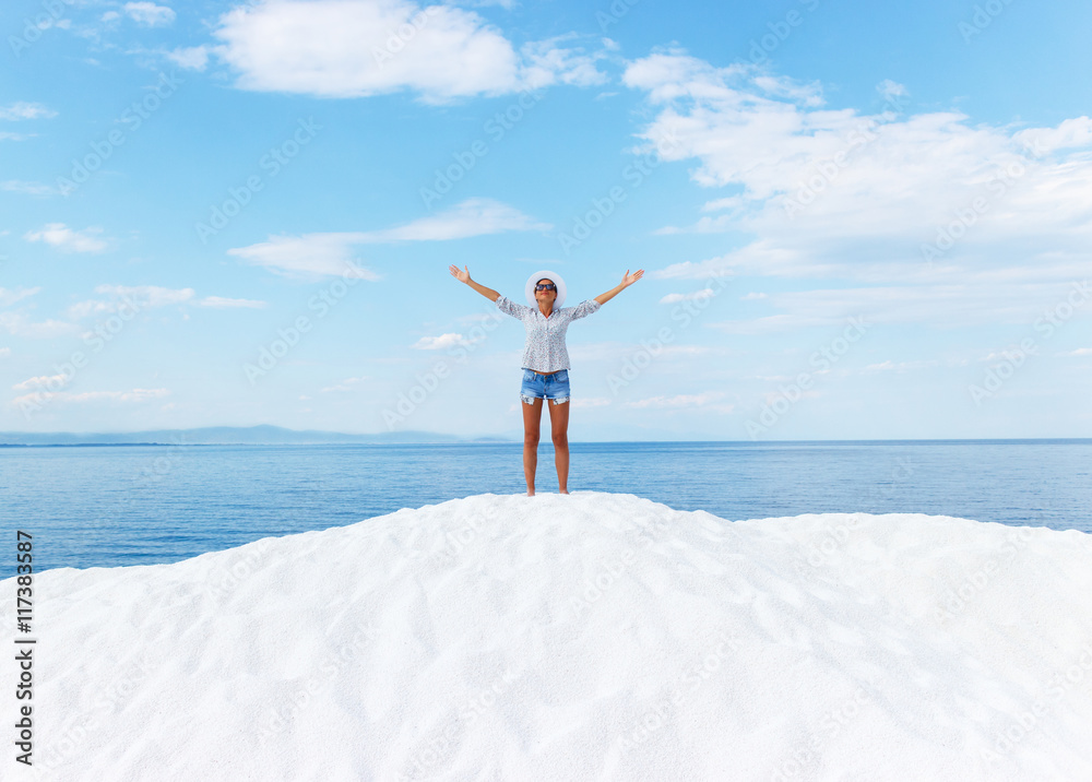 Young woman standing on white beach with her arms outstretched over horizon. She is looking towards the sun. Young woman standing on white beach with her arms outstretched over horizon. She is looking towards the sun.