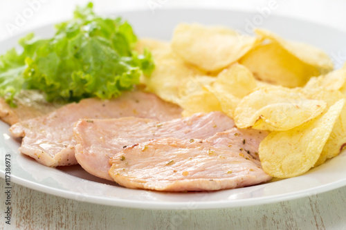 fried meat with potato chips and fresh salad on white dish on white wooden background