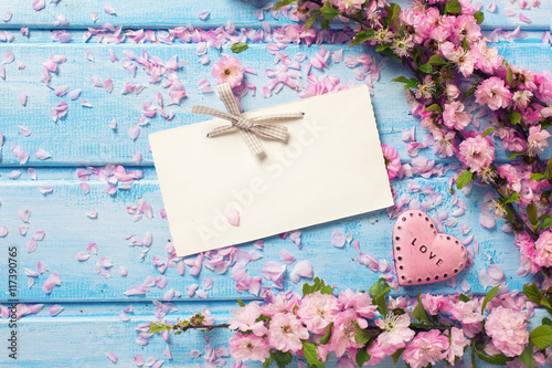Pink sakura flowers, empty tag and heart on blue wooden planks