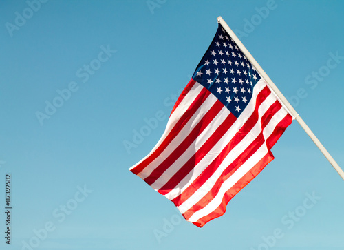 United States flag blows in the wind against a blue sky attached to the wall from the side