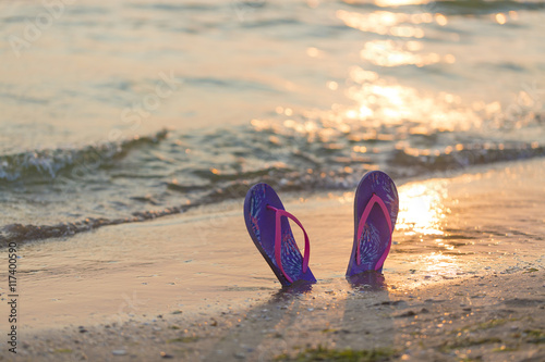 Summer vacation concept. Colorful flip flops on the sandy beach during sunset