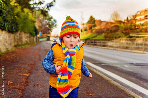 Outdoor portrait of adorable toddler boy wearing colorful hat and scarf, playing outdoors on a nice warm fall day