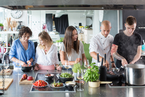 Men cooking and women talking and smiling in modern kitchen photo