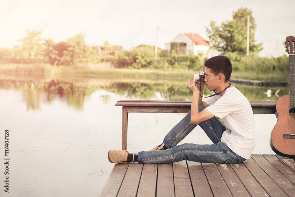 Young photographer sitting on the wooden deck beside the water with sunrise.