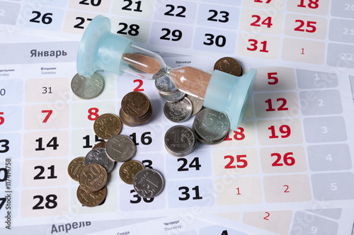 Hourglass on calendar sheets lie near rubles
