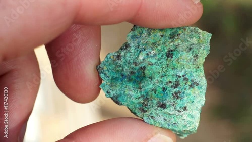 Close up shot of the hand of an anonymous prospector or geologist holding a rock chip sample of copper oxide ore used in the mining industry to extract copper base metal to sell as a commodity.