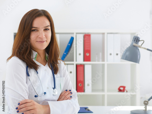 Beautiful female medicine doctor with hands crossed on her chest. She smile and look in camera. Medical care or insurance concept.