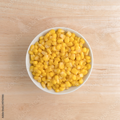 Organic sweet corn in a small bowl atop a wood table top view.