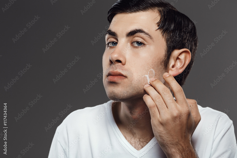 Man applying cream after shave on face over grey background. Man applying cream after shave on face over grey background.