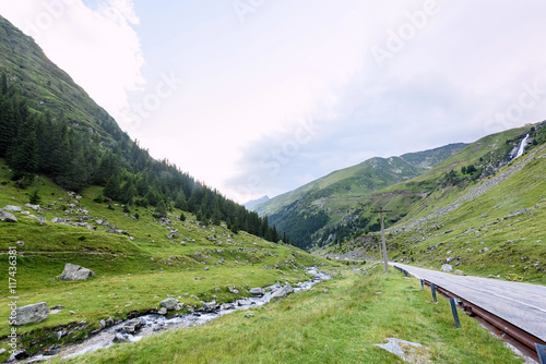 Photo of green capra peak, a road and a small river in fagaras mountains, Romania.