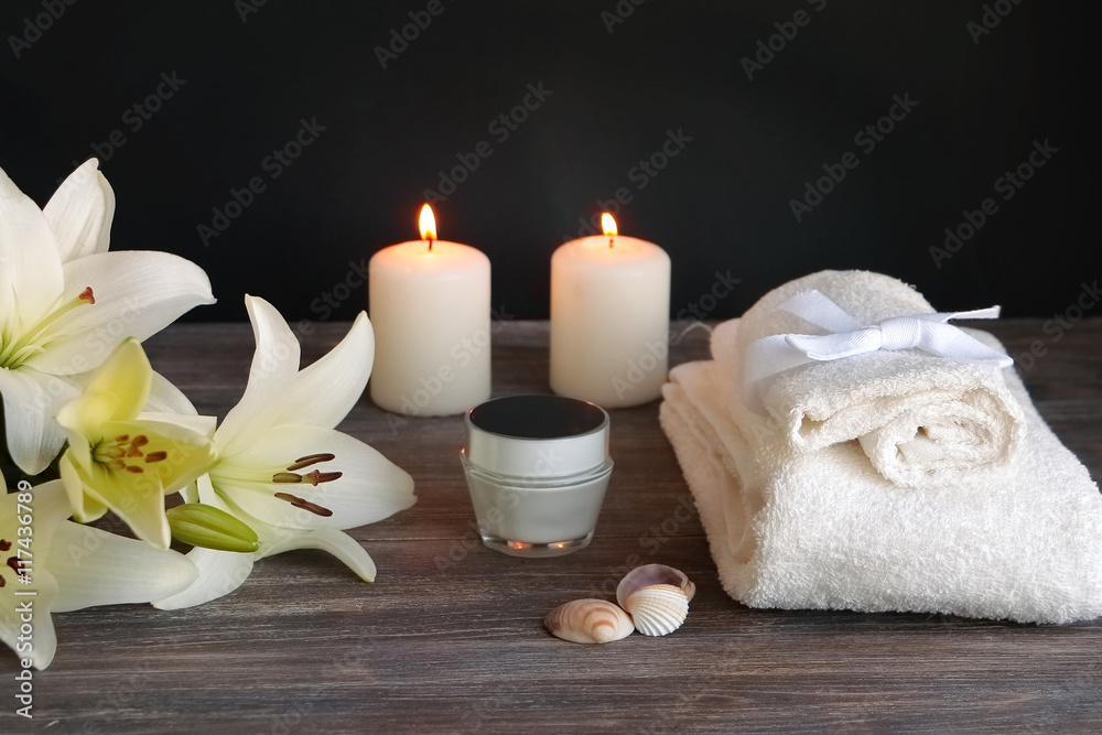 Piece of spa interior with flowers of lily, candles, towels, tissue, napkins, cosmetic product, special light. Copy space.Black background.