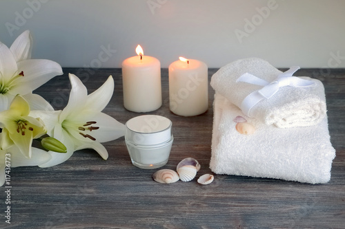 Piece of spa interior with flowers of lily  candles  towels  tissue  napkins  cosmetic product  special light. Copy space. White background.