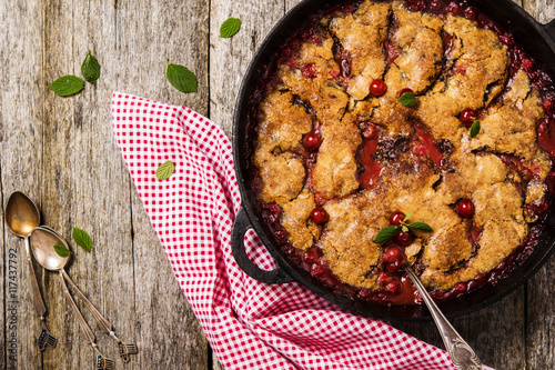 Slika na platnu Cherry Cobbler with cinnamon and chocolate on a rough wooden board with cloth an