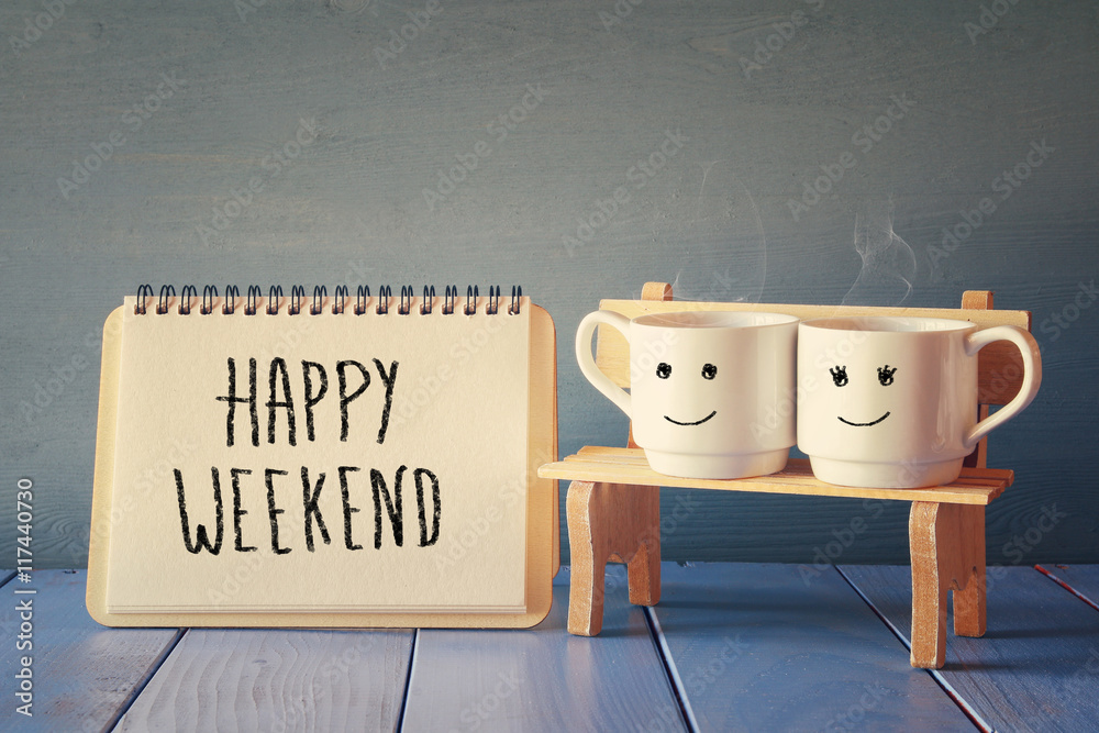 coffee cups next to notebook with phrase "happy weekend" - obrazy, fototapety, plakaty 