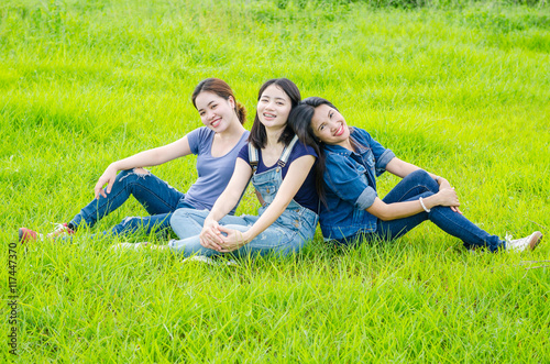 Three beautiful asian women sitting in meadow and smile