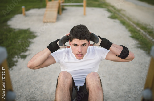 Young man doing sit-ups in a park, outdoors photo