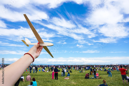Girl holding toy wood plane at an airshow with crowd in the back