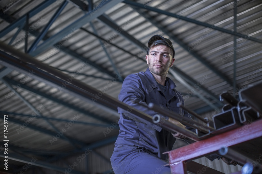 Mechanic in workshop taking steel bar from high rack Mechanic in workshop taking steel bar from high rack