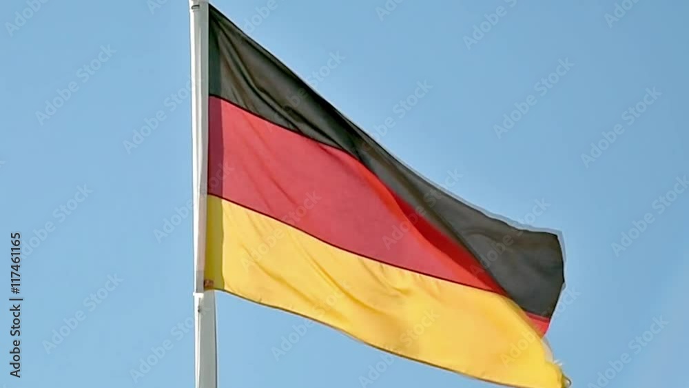A German flag flutters in the wind against a blue sky background A German flag flutters in the wind against a blue sky background