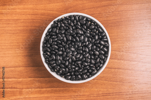 Black beans into a bowl over a wooden table. Phaseolus vulgaris 'Black turtle