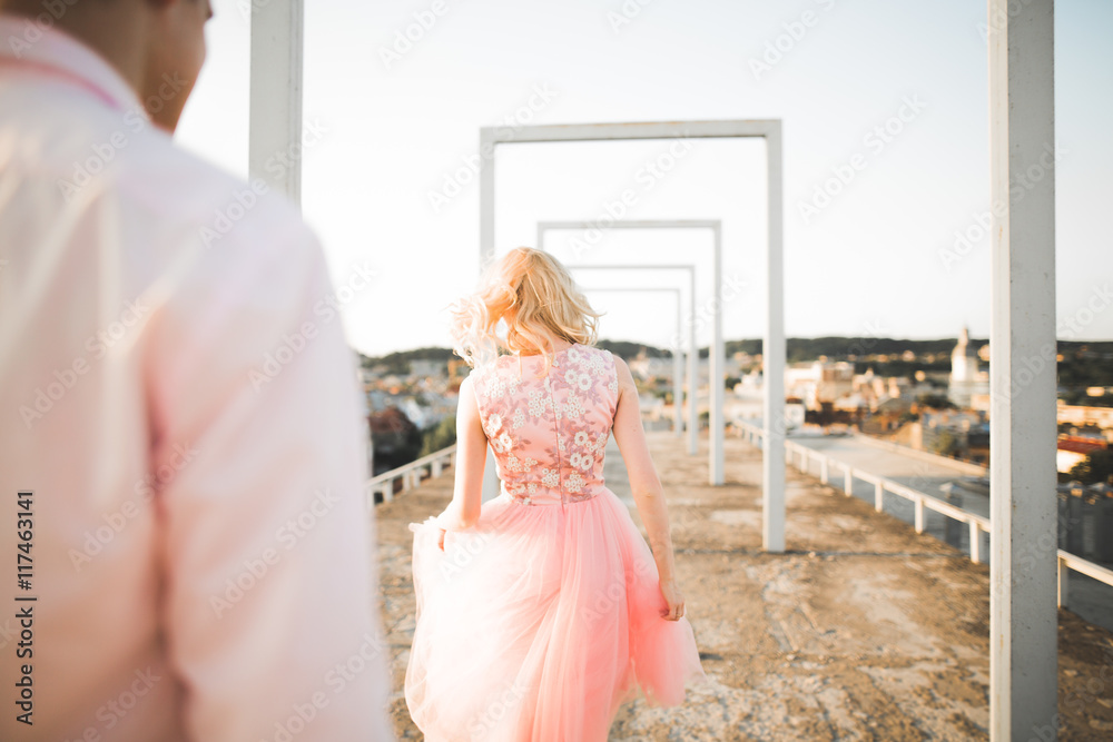 Fototapeta premium Fashion lovely beautiful couple posing on roof with city background. Young man and sensual blonde outdoor. Lifestyle.