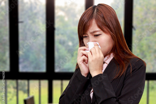 Businesswoman with allergy or cold sneezing into napkin in room