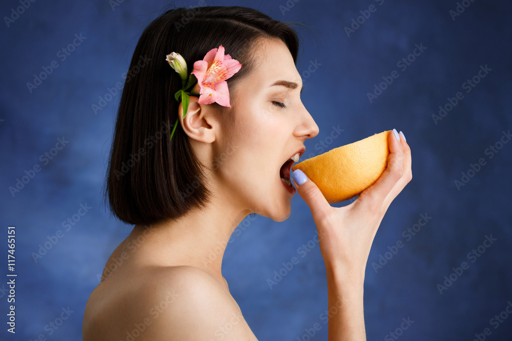 Close up portrait of tender young girl holding cut orange over blue background Close up portrait of tender young girl holding cut orange over blue background