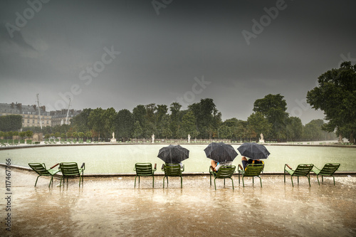 Photography People seating by pond in Jardin Tuileries, saving from hard rain under umbrellas