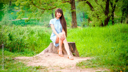 фотографія young woman sitting on stump at summer green park.