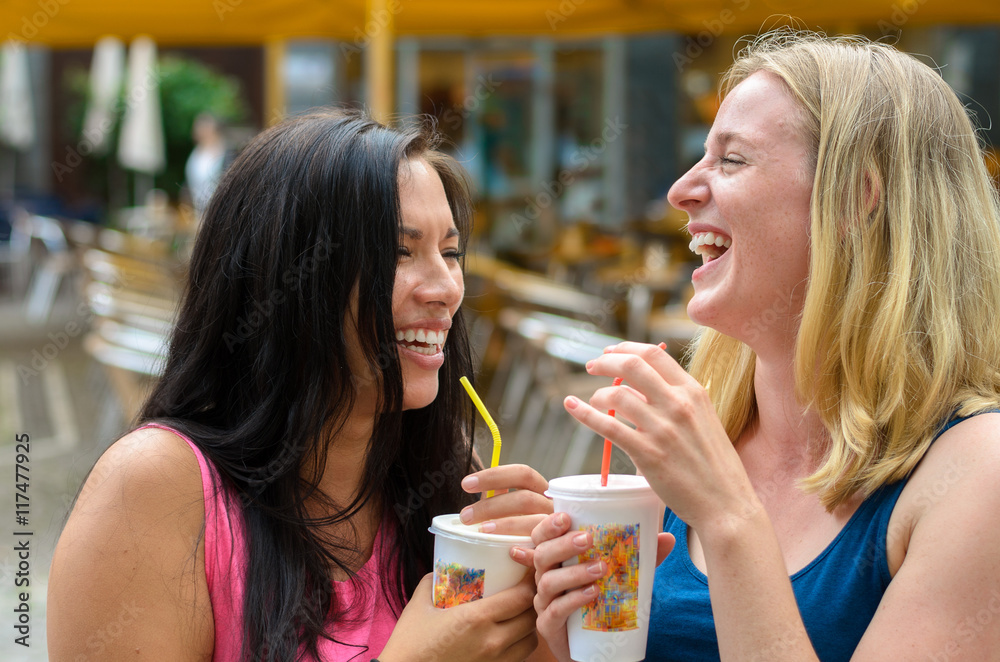 Pair of happy women with drinks while laughing Pair of happy women with drinks while laughing