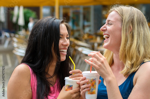 Pair of happy women with drinks while laughing