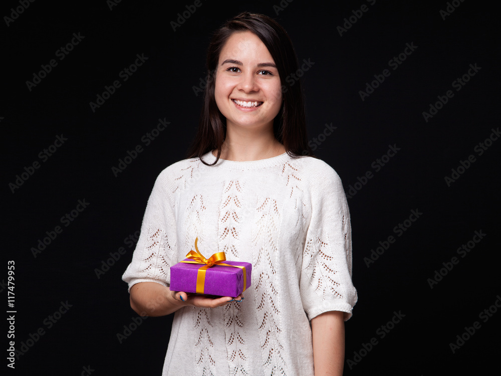 Happy young woman holding a present in the hands, black background Happy young woman holding a present in the hands, black background
