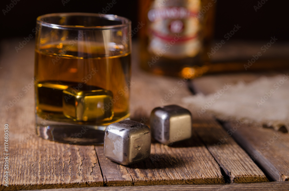 Whiskey glass with stainless steel ice cubes on wooden rustic background. Selective focus.