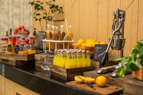  Brunch buffet with fresh orange juice in the bottles. An orange cut on a wooden chopping board and an orange juicer press 