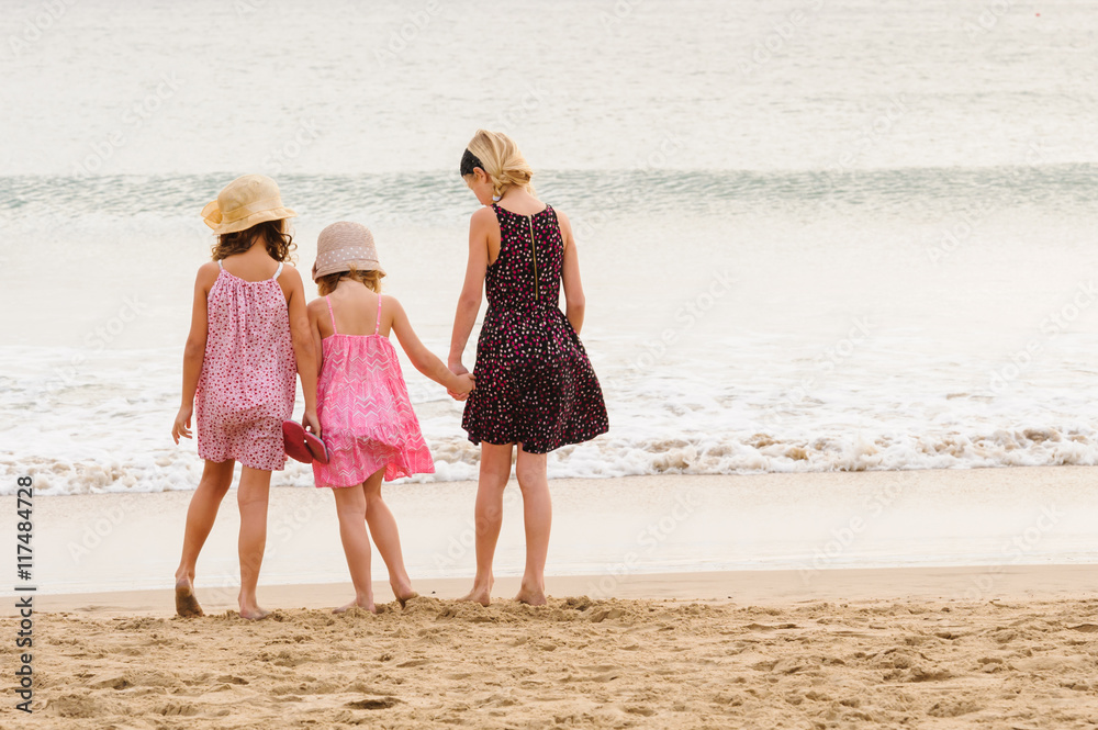 3 sisters stand on beachfront facing the ocean.