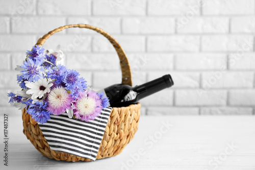 Wine bottle with flowers in basket on light background