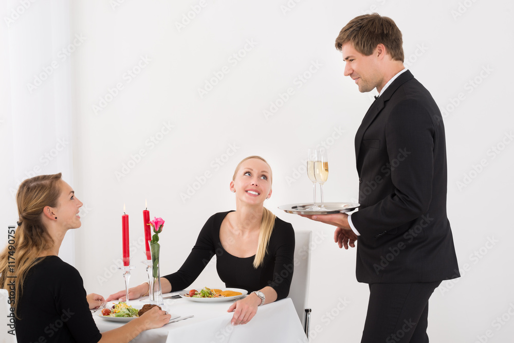 Waiter Serving Glass Of Champagne To Female Friends Waiter Serving Glass Of Champagne To Female Friends