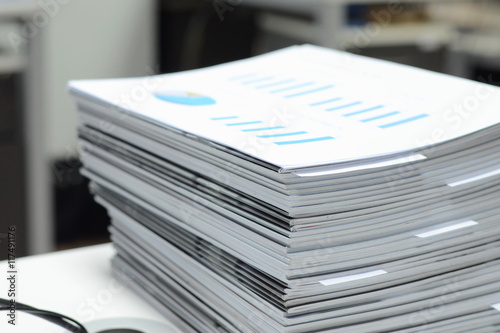 Stack of business reports on desk at workplace with high key tone.

