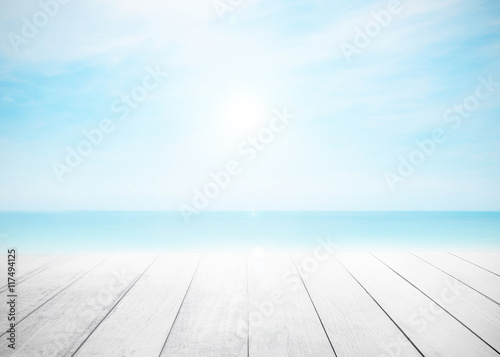 Wood floor with white blue surfing wave background. Blue water on ocean beach and sky bright. Nature wallpaper blur of sea daytime. Focus to wooden in the foreground. Timber pattern texture stage.