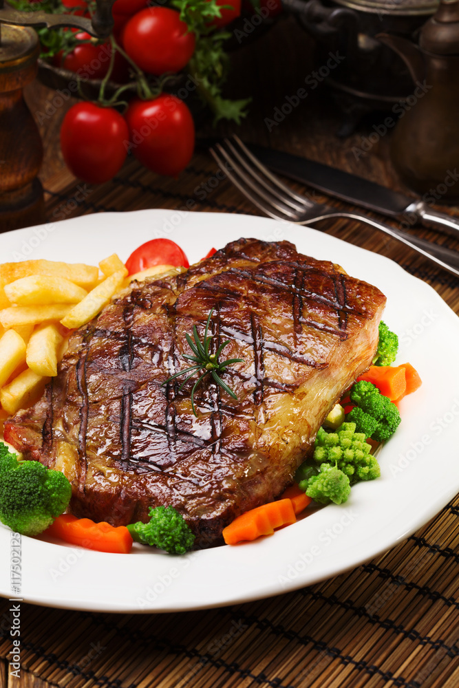 Grilled beef steak served with French fries and vegetables on a